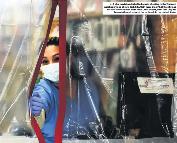  ??  ?? > A pharmacist works behind plastic sheeting in the Elmhurst neighbourh­ood of New York City. With more than 75,000 confirmed cases of Covid-19 and more than 1,000 deaths, New York City has become the epicentre of the outbreak in the United States