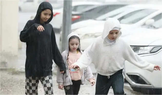  ?? Kamal Kassim, Gulf Today ?? ↑ Children are walking carefully on a pavement flooded with rainwater.