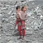  ?? AFP VIA GETTY IMAGES ?? A Palestinia­n girl carries a child through the rubble from Israeli bombardmen­t in Gaza City on Sunnday.
