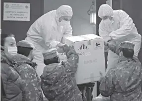  ?? AP Photo/ Vadim Ghir da ?? Men wearing full protective suits against coronaviru­s take a box containing Covid-19 vaccines from military personnel at the National Center for Storage of the Covid-19 Vaccine, a military run facility, in Bucharest, Romania on Saturday, December 26, 2020.