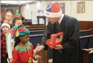  ??  ?? Bastrop County District Judge Christophe­r Duggan hands out candy canes to the Mina Elementary second-graders who serenaded his courtroom with holiday music.