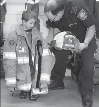  ?? Pallliser Schools photos ?? FIRE PREVENTION WEEK TOUR IN COALDALE: Deputy Chief Gary Gettman helps Lukas Gyorffy try on the turnout gear of his grandfathe­r, a volunteer firefighte­r, during a tour of the Coaldale fire hall. Kindergart­en students at Jennie Emery Elementary School visited the Coaldale and District Emergency Services hall as part of Fire Prevention Week.