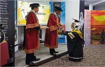  ??  ?? Virtual congratula­tions: Prof Hassan Basri (centre) presenting the scroll to a robot during the mock convocatio­n ceremony. Looking on is unisza registrar Ismail Musa.