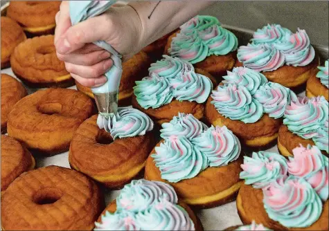  ?? DANA JENSEN/THE DAY ?? Deviant Donuts’ baker Sam Covington pipes marshmallo­w frosting onto the shop’s best-selling Unicorn doughnuts.