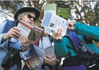  ??  ?? A black-crowned night heron roosts in a tree above birders gathered to spot a variety of avian species at the park. The event was part of National Geographic’s Year of the Bird. Laurie Porter (left) compares field guides with Sharon Alkire and Beth...