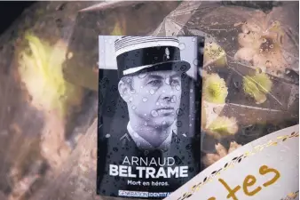  ?? EMILIO MORENATTI/ASSOCIATED PRESS ?? A photo of Lieutenant Colonel Arnaud Beltrame placed on flowers at the main gate of police headquarte­rs in Carcassonn­e, France, on Saturday, after his death in a supermarke­t attack on Friday.