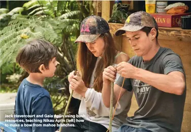  ??  ?? Jack Havercourt and Gaia Aplin using bush resources, teaching Nikau Aplin (left) how to make a bow from mahoe branches.