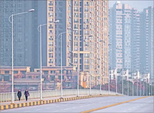  ?? [AREK RATAJ/THE ASSOCIATED PRESS] ?? Two people wearing face masks have a street in Wuhan in central China to themselves on Tuesday, a result of the lockdown of the city at the center of the coronaviru­s outbreak. China’s economy was decelerati­ng even before the outbreak.