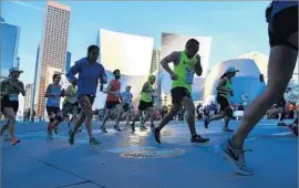  ?? Christina House For The Times ?? MARATHON participan­ts pass Disney Hall in downtown L.A. on their way to the finish line. The race route began at Dodger Stadium and ended in Santa Monica.