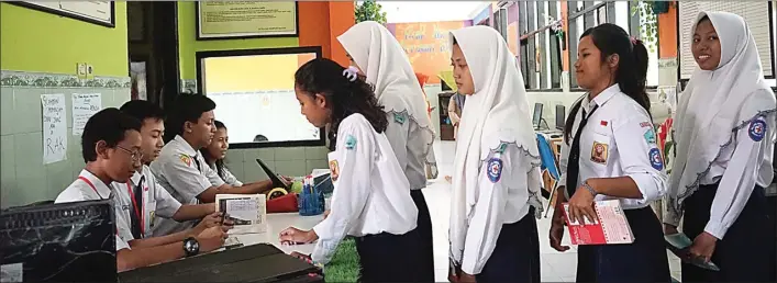  ?? SHELA TAMARA/JAWA POS ?? TERTIB: M. Aril Asyhari (kiri), petugas perpustaka­an sekaligus siswa kelas 8-A, melayani peminjaman buku di perpustaka­an SMPN 2 Sedati kemarin. Siswa yang nyerobot antrean tidak akan dilayani.