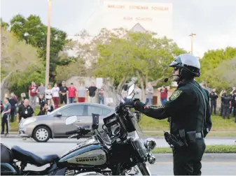  ?? Terry Renna / Associated Press ?? A police officer stands watch last month as students return to Marjory Stoneman Douglas High School in Parkland, Fla. A gunman killed 17 students and staff at the school on Feb. 14.