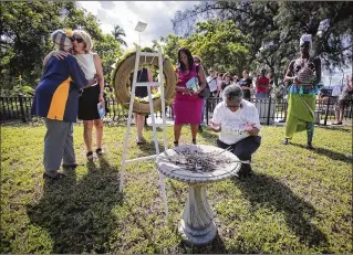  ?? PHOTOS BY BRUCE R. BENNETT / THE PALM BEACH POST ?? Betty Lou McCray-Wells (left) hugs Mayor Jeri Muoio as Dorothy Hazard (second from right) kneels during a wreath laying Saturday at the mass burial site for 674 victims of the hurricane of 1928 at Tamarind Avenue and 25th Street in West Palm Beach.