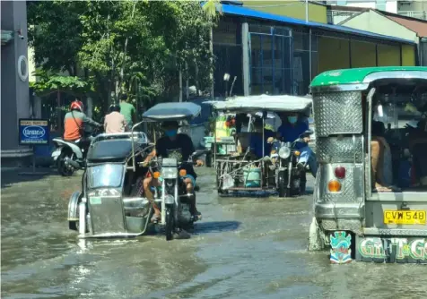  ?? FLOODED ROAD. (Chris Navarro) ?? Tricycles and passenger jeepneys traverse the Apalit-Macabebe road as rain and high tide caused flooding in the area over the weekend..