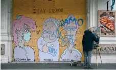  ??  ?? A man paints a picture near a boarded-up shopfront decorated with a graffiti mural on the coronaviru­s crisis, in central London yesterday. Many businesses in the UK are getting ready to reopen on Monday.