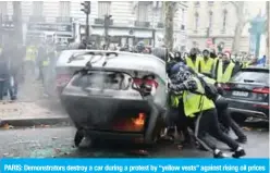  ?? — AFP ?? PARIS: Demonstrat­ors destroy a car during a protest by “yellow vests” against rising oil prices and living costs on the Champs-Elysees yesterday.