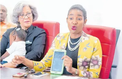  ?? CONTRIBUTE­D ?? Gracie Moss-Solomon (right), principal, Union Gardens Infant School, addresses the gathering as Kim Mair, chief executive officer, JMMB Joan Duncan Foundation, holds a sleeping Adrianna McKnight during yesterday’s launch of the One Tab In Schools Initiative GoFundMe page.