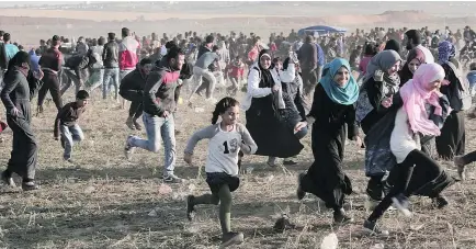  ?? — THE ASSOCIATED PRESS ?? Palestinia­n protesters run for cover from tear gas fired by Israeli soldiers during clashes with Israeli troops along the Gaza Strip border with Israel, east of Beit Lahiya, on Saturday.