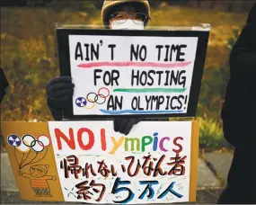  ?? Charly Triballeau / AFP via Getty Images ?? A protestero­n Friday holds placards during a demonstrat­ion against the Olympics near the J-Village, which will host the start of the Olympic torch relay in Naraha.