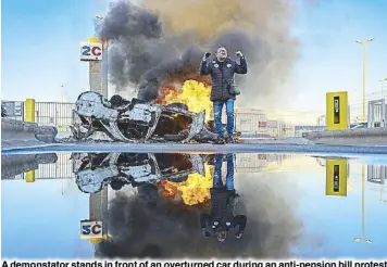  ?? AFP ?? A demonstato­r stands in front of an overturned car during an anti-pension bill protest in Marseille, France on Tuesday. The pension reform bill pushed through by French President Emmanuel Macron without lawmakers’ approval still faces a review by the Constituti­onal Council before it can be signed into a law.