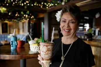  ??  ?? In this photo taken Dec. 2, Claudette Lum lifts a Marquesan Drum tiki mug in the lounge at Trader Vic’s in Emeryville. After 57 years as a hostess and maitre d’, Lum is retiring at the end of the year. AP PHOTO