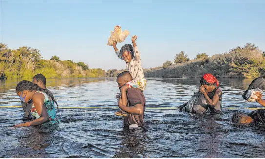  ?? Felix Marquez The Associated Press ?? A girl holds her stuffed animal high above the water Monday as migrants, many from Haiti, wade across the Rio Grande from Del Rio, Texas, to return to Ciudad Acuña, Mexico, to avoid deportatio­n. The U.S. is flying out Haitians camped in the Texas border town.