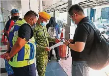  ??  ?? 志愿警卫团员先检查乘­客的警方批准信，才放行进入码头候船室。