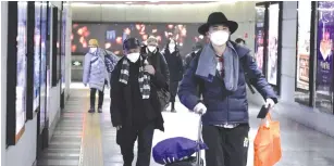  ?? (Jason Lee/Reuters) ?? PEOPLE WEARING masks walk through an undergroun­d passage to the subway in Beijing on Tuesday.