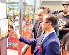  ??  ?? Tsang (left) guiding Lim to gain entry into EZY Box, Malaysia's first unmanned store, with the WeChat applicatio­n on his smartphone at KK Times Square.