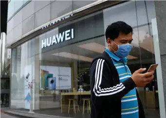 ??  ?? TENSIONS RISING: A man wearing a face mask uses his mobile phone as he walks past a Huawei store in Beijing on Saturday. At left, attendees walk past a display for 5G services from Chinese technology firm Huawei at the PT Expo in Beijing last year.