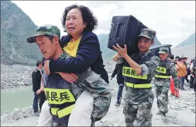  ??  ?? Reserve soldiers on Sunday carry victims and their belongings from Xinmo village on the road to safety. They were stuck on the mountain because of the landslide.