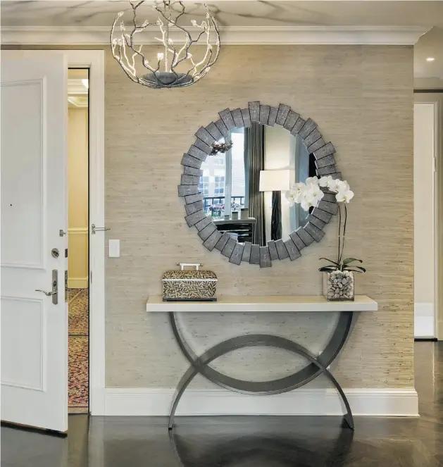 ?? Francis Dzikowski/ ESTO Photograph­ics ?? A restrained touch — including a neutral grasscloth for the walls and light console and chandelier — makes a well-appointed entrance that is cohesive and calming.