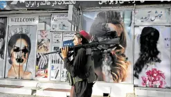  ?? —AFP ?? CHANGE OF IMAGE A Taliban fighter walks past a beauty salon in Kabul with images of women painted over.