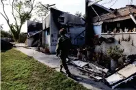  ?? (Ronen Zvulun/Reuters) ?? A SOLDIER passes the remains of burnt houses in Kibbutz Be’eri in the South yesterday.