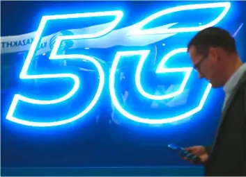  ?? — AFP photo ?? A man uses his phone next to a 5G hotspot sign at the Mobile World Congress (MWC) in Barcelona. Unlike upgrades of wireless networks in the past, 5G will deliver not just faster phone and computer data but also help connect up cars, appliances, cargo and crop equipment.