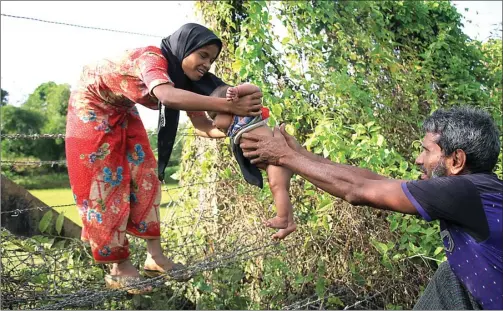  ?? REHMAN ASAD/AFP PHOTO ?? DEMI ANAK: Seorang laki-laki menyerahka­n bayi kepada perempuan melewati kawat berduri di perbatasan Myanmar dan Bangladesh saat melarikan diri dari aksi represif militer Myanmar.