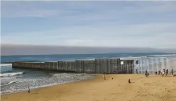  ?? (Jorge Duenes/Reuters) ?? PEOPLE ARE seen next to a wall separating Mexico and the United States last month while an artist paints part of it, as seen from Playas Tijuana, Mexico.