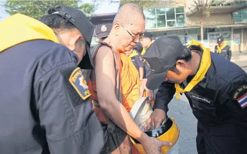  ?? WICHAN CHAROENKIA­TPAKUL ?? ABOVE Officials stop a monk at Wat Phra Dhammakaya and search his belongings at an entrance to the temple.