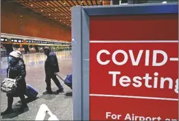  ?? CHARLES KRUPA VIA AP ?? TRAVELERS PASS A SIGN near a COVID-19 testing site in Terminal E at Logan Airport, on Dec. 21, 2021, in Boston.