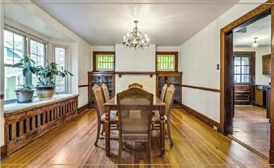  ??  ?? The dining room has a long window seat, hardwood floors and a decorative fireplace flanked by stained-glass windows and built-in cabinets with leaded-glass doors.