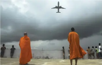  ?? — AFP ?? Buddhists monks and children look out from the rooftop at a Buddhist mission hostel and school for underprivi­leged children as an internatio­nal passenger flight takes off from the Netaji Subhash Chandra Bose Internatio­nal Airport as the authoritie­s eased restrictio­ns in Kolkata on Sunday.