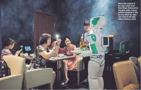  ??  ?? Diners take pictures of the robot waiter at the Robot Magic Restaurant in Shanghai, while a human waitress stands by to take the tray, which the robot can’t lower to the table without making a mess.