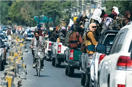  ?? AFP ?? A man on his bicycle rides past a convoy of Taliban fighters patrolling along a street in Kabul on Thursday. The Taliban are preparing to unveil their new government.