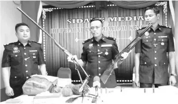  ??  ?? Douglas showing the home-made gun (left) confiscate­d by police from the suspect, and an air rifle (right) discovered at the roadside by an enforcer of a company in Sook. Also seen are the investigat­ing officers of the case.