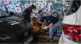  ?? ?? Nascimento (right) and medical students provide medical treatment to a homeless woman with her hand injured inside a homeless encampment located under the Madureira viaduct, in north Rio.