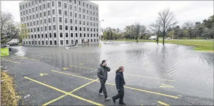  ?? CP FILE PHOTO ?? People walk past the flooded parking lot of the Pebb Building, located across from the Ottawa River, following a rain storm in Ottawa on Oct. 30.