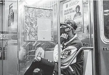  ?? JOHNNY MILANO/THE NEW YORK TIMES ?? The poem “Cranes in August,” by Kim Addonizio, is seen next to a masked commuter on a subway car in New York.