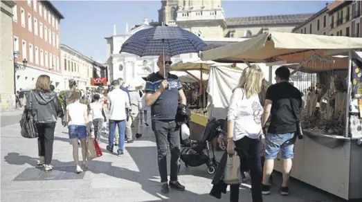  ?? NURIA SOLER ?? Protegido ▷ Un viandante se parapeta bajo un paraguas del sol en su visita al mercado de las tres culturas de Zaragoza.