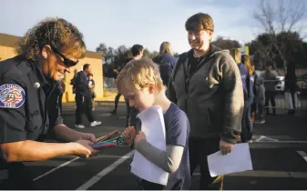  ??  ?? Above: First-grader Silas Kalstad, 6, chooses a pencil from firefighte­r Cyndi Foreman as his mother, Gretchen Emmert, looks on. First responders came to welcome the students back to school.