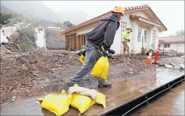  ?? Photograph­s by Al Seib Los Angeles Times ?? JASON RIVAS places sandbags in front of homes on San Como Lane in Camarillo Springs, where residents are under a voluntary evacuation order. Two mudslides in 2014 badly damaged or destroyed 10 homes.
