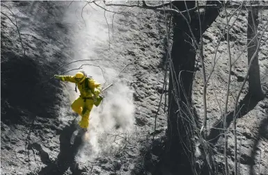  ?? Leah Millis / The Chronicle ?? Xavier Lugo of Cal Fire’s Mariposa unit scurries down a steep, ashy slope after working with his crew to put out hot spots at the Tassajara Fire near Big Sur in Monterey County, which started Saturday.